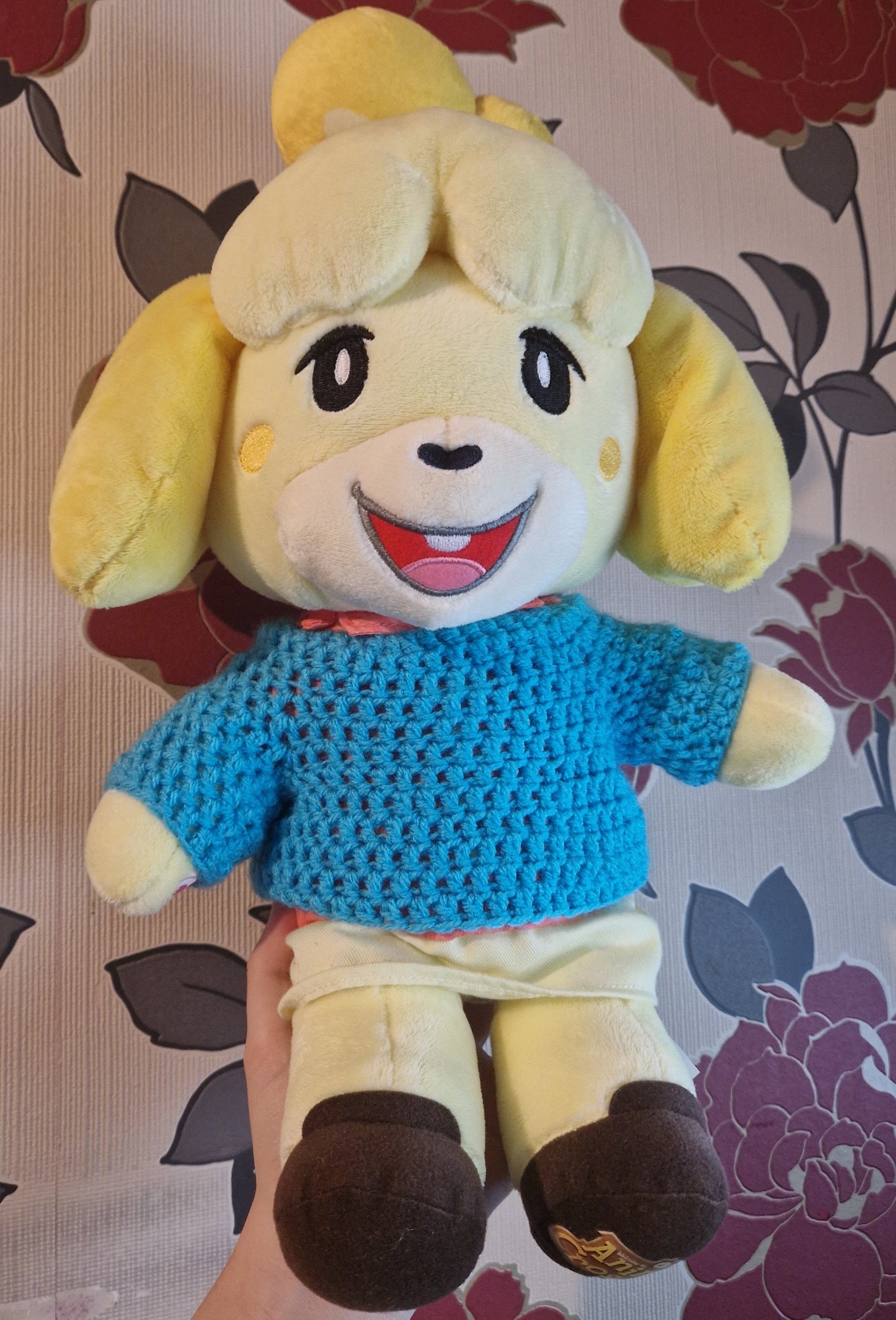 Plush toy with a blue sweater on a floral-patterned background